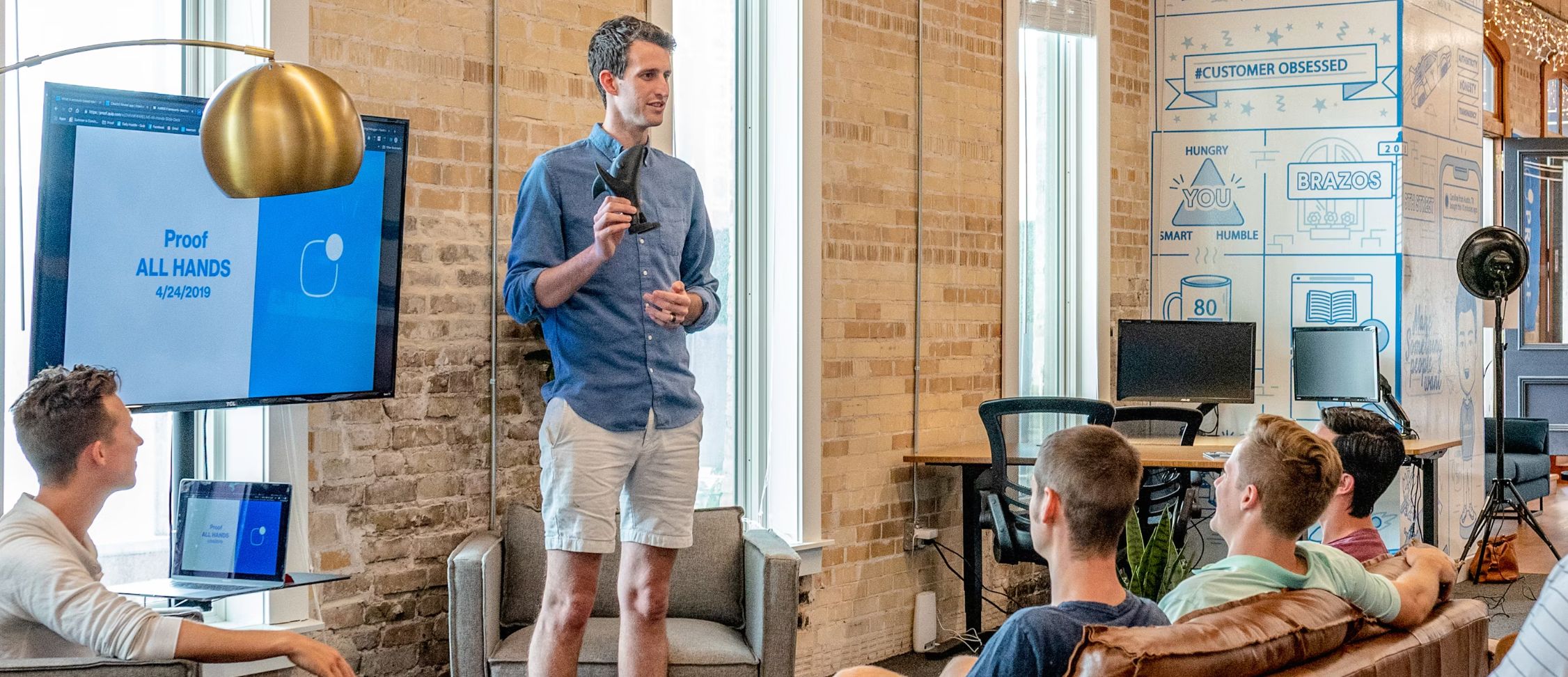 A presenter speaking to a team in a brick-walled office