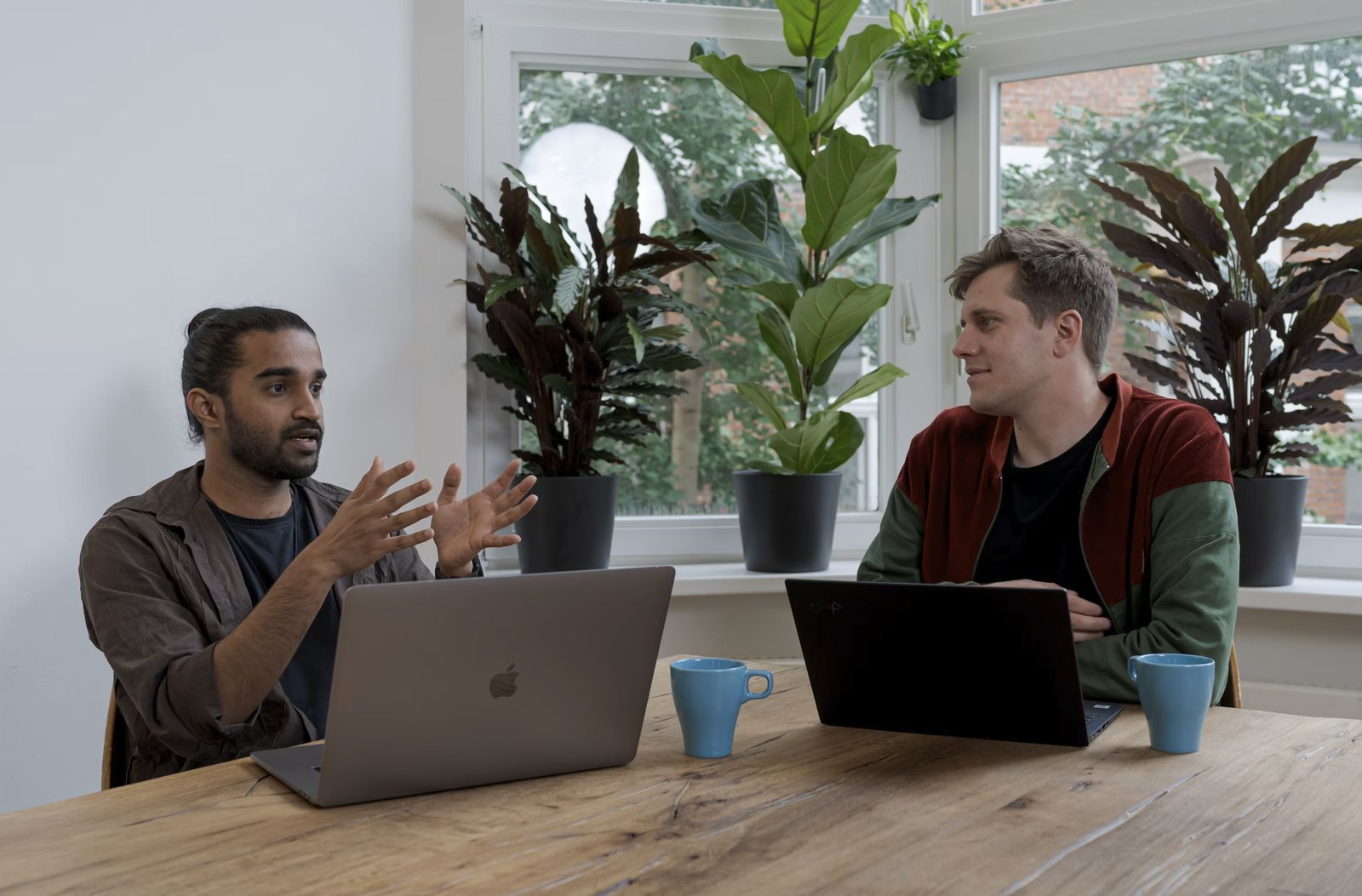 Two colleagues talking at a table with laptops